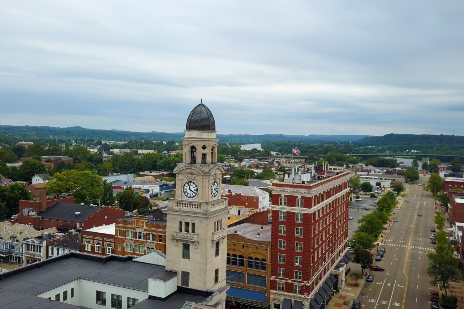Downtown clock tower with domed cupola overlooking river, bridge and tree-lined streets, urban backdrop for American industry