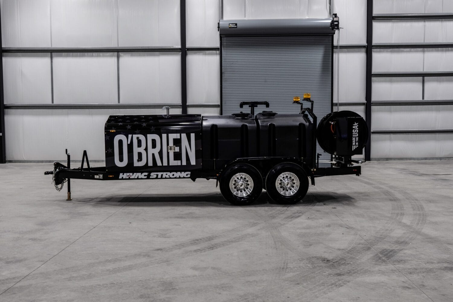 O'Brien Sewer Jetters trailer-mounted sewer jetter with dual axles, hose reel, and tanks in a factory bay.