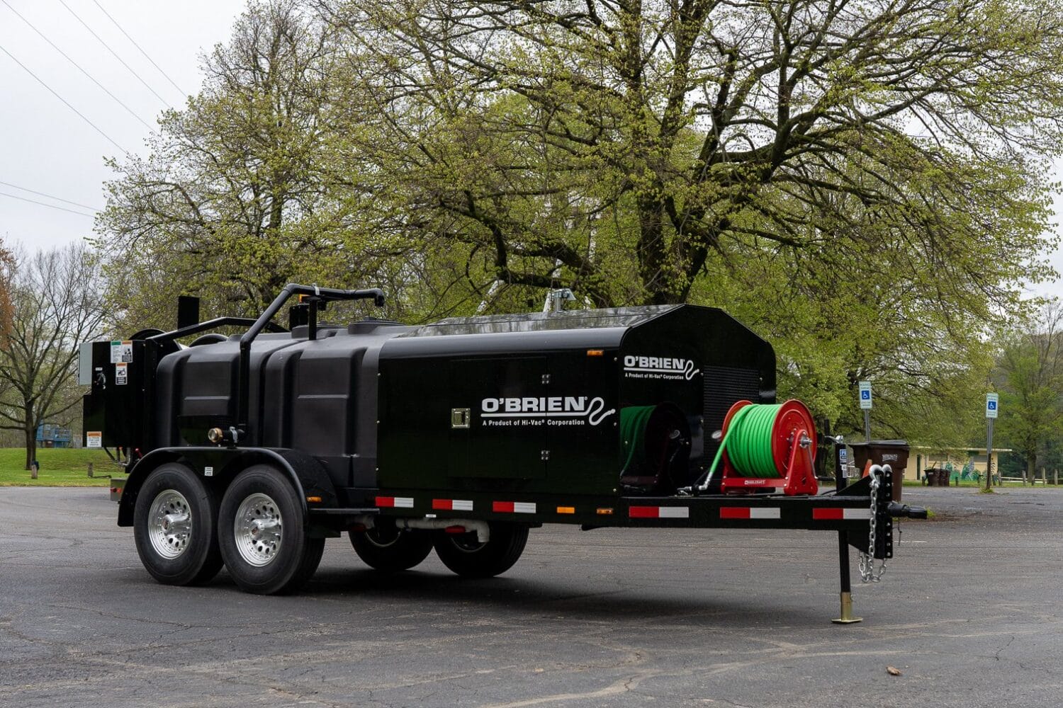 O'Brien Sewer Jetters trailer unit with water tank and green/red hose reels parked under spring trees.