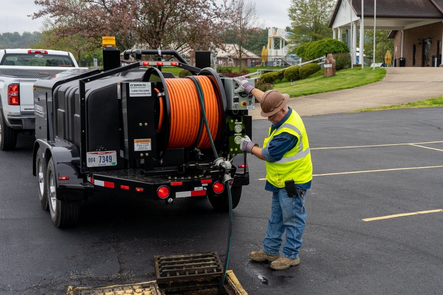 O'Brien Sewer Jetters trailer-mounted hydro jetter clearing a parking lot storm drain, operator at controls.