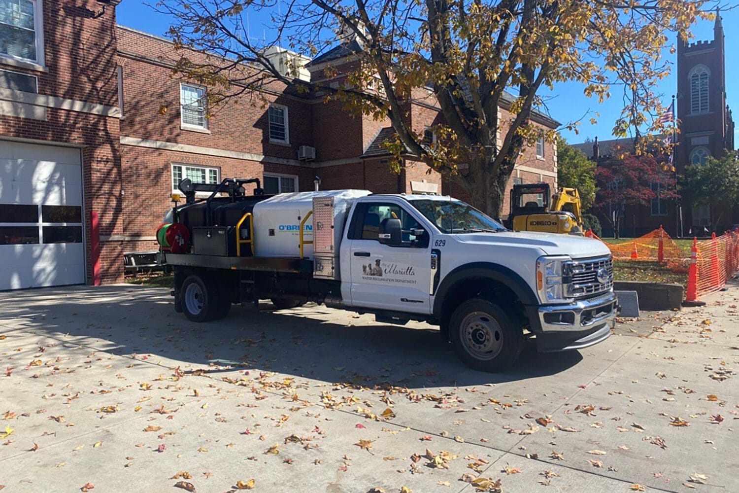 Municipal flatbed with O'Brien Sewer Jetters unit with water tank and hose reel, parked at a street excavation site.