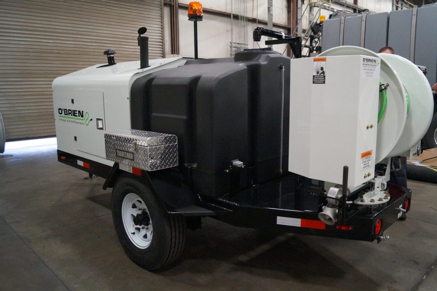 O'Brien Sewer Jetters trailer-mounted sewer jetter with hose reel, water tank, and toolbox on the factory floor.